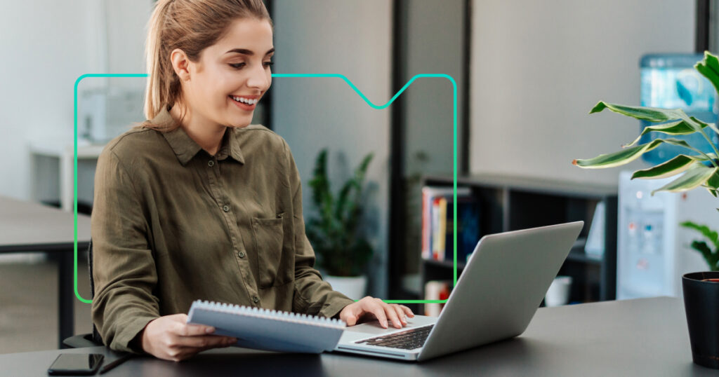 a woman working at a laptop with a notebook, with a synergy learning brand device behind her