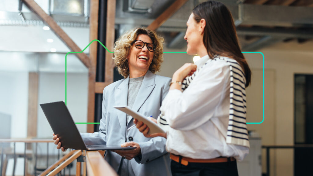 two female colleagues laughing while working on a laptop and table device