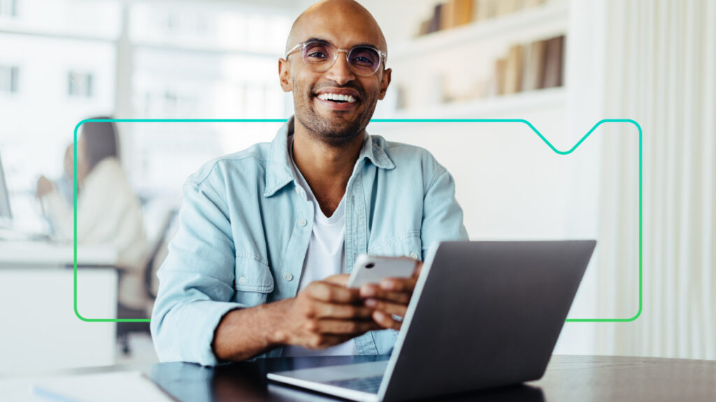 Man holding a mobile phone working at a laptop