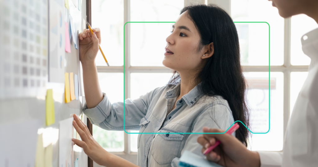 Frau, die auf einem Whiteboard schreibt, mit dem Gerät der Marke synergy learning im Hintergrund