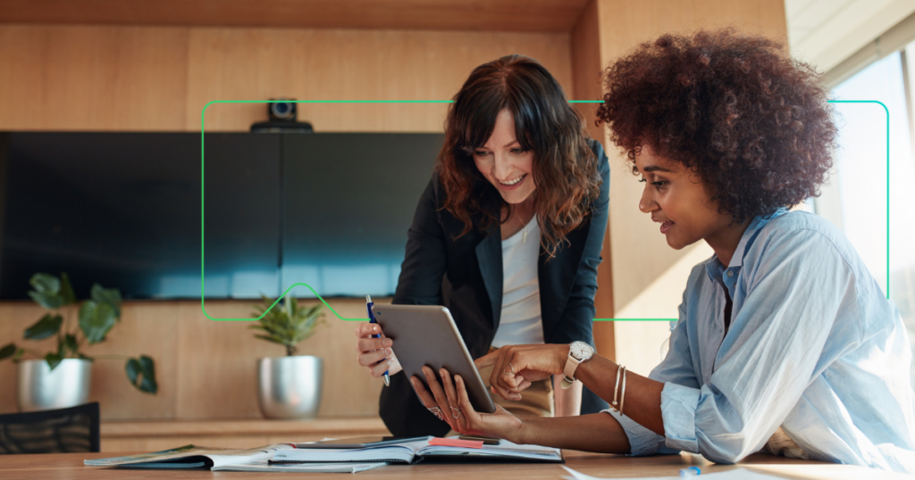 zwei Frauen, die mit einem Tablet arbeiten, hinter ihnen ein Gerät der Marke synergy learning