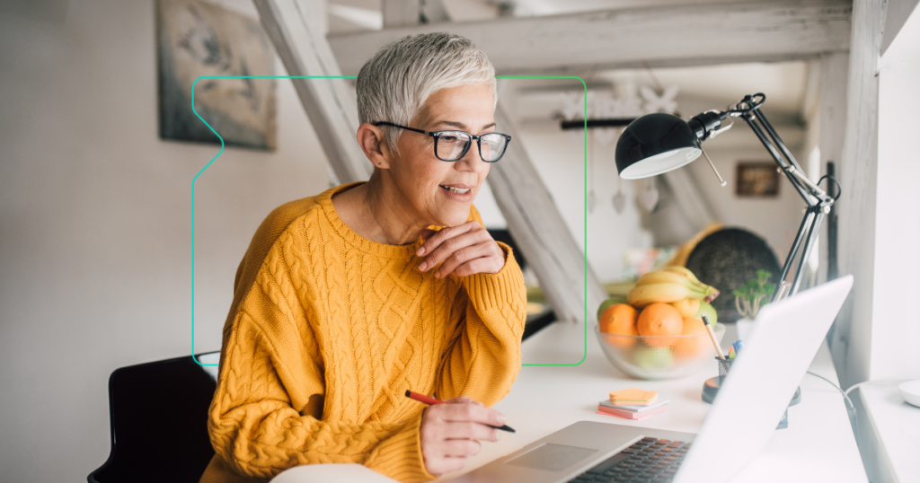 eine Frau mittleren Alters, die an einem Laptop arbeitet und hinter sich ein Gerät der Marke synergy learning hat